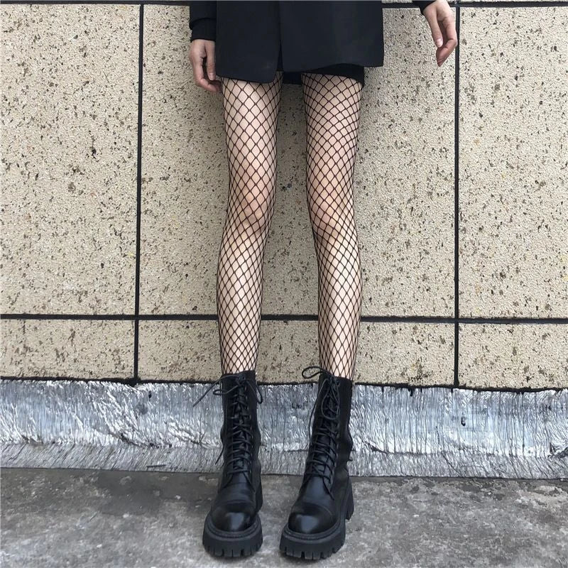Person wearing black fishnet tights and black boots against a tiled wall.