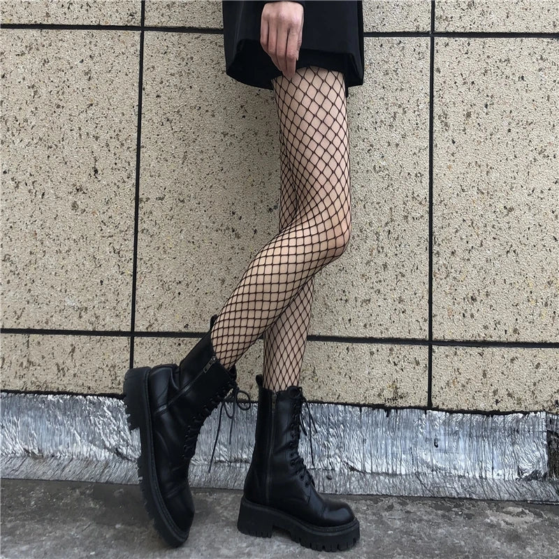 Person wearing black combat boots and fishnet stockings against a tiled wall.
