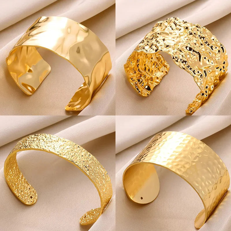 Four gold cuff bracelets on a beige fabric background