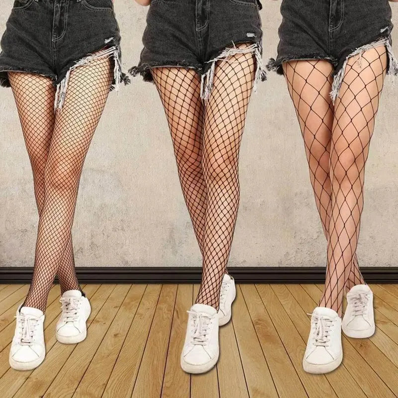 Three pairs of legs wearing fishnet stockings and white sneakers on a wooden floor.