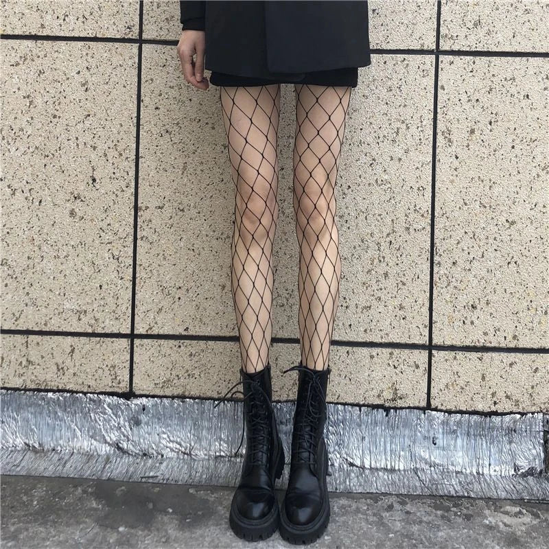 Person wearing fishnet stockings and black boots against a tiled wall.